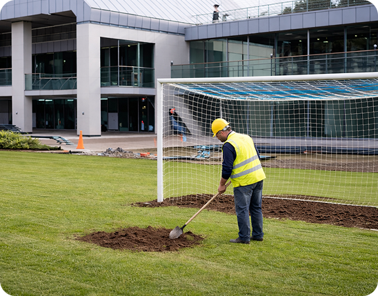 Werker in gele hesje graaft op voetbalveld bij nieuw gebouw — modernisering van accommodatie